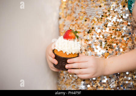 Piccola ragazza in un abito scintillante holding bella tortina, vicino. Panificio, cibo dolce e concetto di persone. Deliziosi muffin su sfondo spumanti Foto Stock