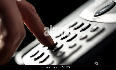 Primo piano del dito di un imprenditore di effettuare una chiamata su una linea telefonica fissa premendo i pulsanti sulla tastiera per comporre il numero. Foto Stock