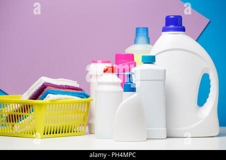 Foto di bottiglie di detersivi e multi-colore di asciugamani in cesto isolati su viola, sfondo blu Foto Stock