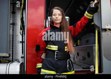 Foto del giovane fire donna con capelli lunghi in tuta guarda in telecamera accanto al motore Fire Foto Stock