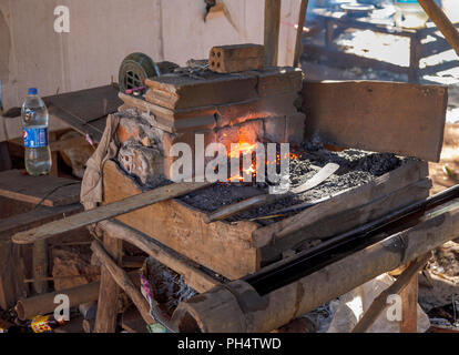 Rosso brillante di carbone caldo sparato forge rendendo machete in Houayhe, un fabbri' village in Bolaven Plateau, provincia di Champasak, Laos, SE Asia Foto Stock