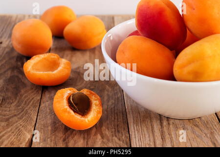 Fresche albicocche in una ciotola bianco, sul tavolo di legno, uno di albicocche tagliate a metà Foto Stock