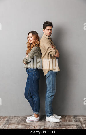 A piena lunghezza Ritratto di un sconvolto coppia giovane in piedi di schiena con le braccia incrociate isolate su grigio Foto Stock