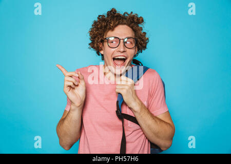 Foto di hipster geek uomo con capelli ricci con gli occhiali e zainetto sorridente e gesticolando a parte isolate su sfondo blu Foto Stock