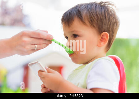 Baby per mangiare il pranzo mentre guardando lo smartphone Foto Stock