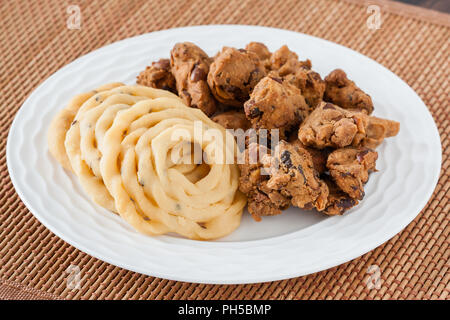 Indian murukku pakoda e snack - un primo piano della tradizionale profondo fritto indiano murukku spuntini e dadi pakkoda su una piastra. Foto Stock