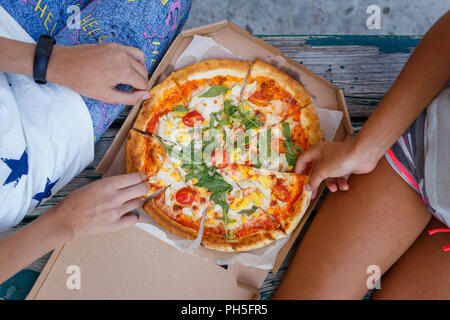 Due ragazze di mangiare la pizza insieme all'aperto. Top visualizza immagine di estate concetto attrezzate Foto Stock