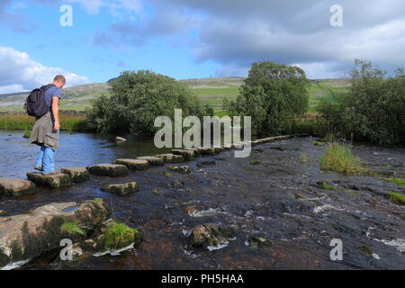 Un turista passeggiate attraverso pietre miliari sul fiume Dow vicino Ingleton nel Yorkshire Dales National Park. Foto Stock