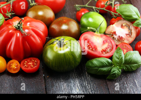 Varie colorato i pomodori e le foglie di basilico sul tavolo rustico. fresche deliziose zebra pomodoro e ccor de boeuf Foto Stock