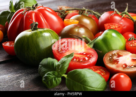 Varie colorato i pomodori e le foglie di basilico sul tavolo rustico. fresche deliziose zebra pomodoro e ccor de boeuf Foto Stock