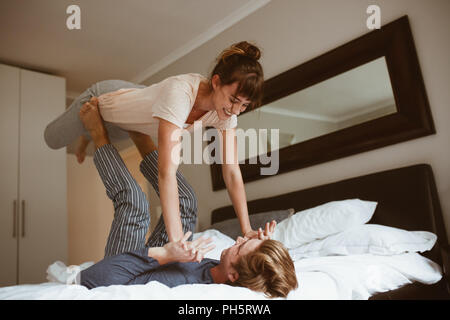 Coppia felice giocando a letto e divertirsi. Uomo disteso sul letto e sollevando la moglie con i suoi piedi tenendo le sue mani. Foto Stock