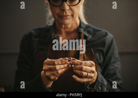 Chiusura del gioielliere femmina mani esaminando l'anello in argento in officina. Donna orafo di ispezione di gioielli. Foto Stock