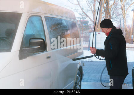 Un uomo bagna un furgone bianco, un uomo bagna un furgone ad un lavaggio auto in inverno Foto Stock