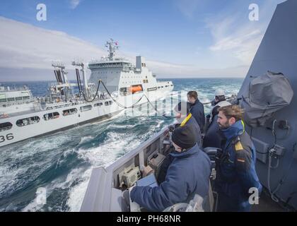 Mare di Norvegia (26 giugno 2018) i marinai a bordo guidato-missile destroyer USS Farragut (DDG 99) osservare il combustibile essendo trasferito alla nave durante un rifornimento in corso con la British Royal ausiliario della flotta di navi cisterna di rifornimento RFA Tidespring (A136). Farragut è attualmente implementato come parte di Harry Truman Carrier Strike gruppo. Con USS Harry Truman (CVN 75) come ammiraglia, distribuito strike gruppo unità includono staffs, di navi e di aeromobili di Carrier Strike gruppo Otto (CSG 8), Destroyer Squadron due otto (DESRON 28) e Carrier aria Wing uno (CVW-1); come pure Sachsen-tedesco di classe F Foto Stock