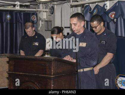 5TH FLOTTA AREA DI OPERAZIONI (30 giugno 2018) della Cmdr. Paolo Tremblay, nave il cappellano, conduce nella preghiera durante una cerimonia per il XVII anniversario della messa in servizio del Wasp-classe assalto anfibio nave USS Iwo Jima (LHD 7), 30 giugno 2018. Iwo Jima è distribuito negli Stati Uniti Quinta Flotta area di operazioni a sostegno di operazioni navali per garantire stabilità marittimo e la sicurezza nella regione centrale di collegamento del Mediterraneo e del Pacifico attraverso l'Oceano Indiano occidentale e tre strategici punti di strozzatura. Foto Stock