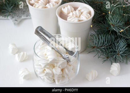 Il cacao con marshmelow in bianco tazze e marshmallows in un vasetto di vetro su un tavolo bianco con rami di abete e la ghirlanda. Foto Stock