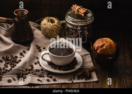 Tazza di caffè sulla tovaglia con Cupcake e spezie varie. Foto Stock
