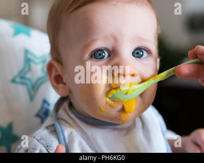 Adorable baby boy con gli occhi blu di mangiare il pranzo da vicino Foto Stock