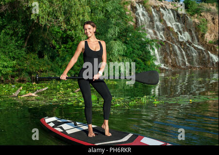 Atletica Giovane donna fare fitness in una scheda con un remo sulle rive di un fiume Foto Stock