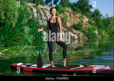 Atletica Giovane donna fare fitness in una scheda con un remo sulle rive di un fiume Foto Stock