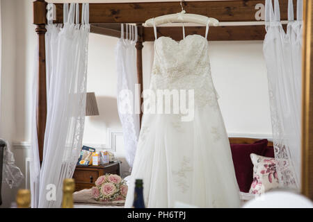 Abito da sposa appeso su un letto a baldacchino in attesa di essere indossato da una sposa il giorno delle nozze, prese alla luce del giorno in una camera da letto Foto Stock