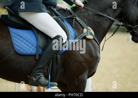 Close-up, dettaglio, gamba, show jumping rider, pantaloni bianchi, in pelle nera stivali da cavallo, seduto sul cavallo, evento arena, persone Foto Stock