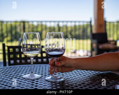 Donna di braccio per raggiungere quasi vuoto bicchieri di vino rosso e bianco su un patio esterno tabella Foto Stock