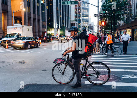 La città di New York, Stati Uniti d'America - 21 Giugno 2018: corriere ispanica sulla bicicletta in crosswalk nella città di New York al crepuscolo Foto Stock