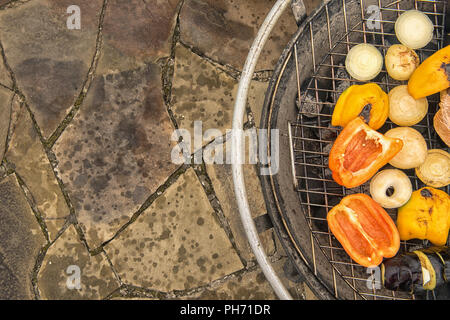Assortimento di verdure grigliate sulla griglia metallica di round grande grill esterno permanente sulla pietra naturale pavimentazione. Mangiare sano concetto. Messa a fuoco selettiva Foto Stock
