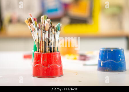 Pentole di artista della vernice usata spazzole su un banco di scuola fotografata nella scuola d'arte Foto Stock