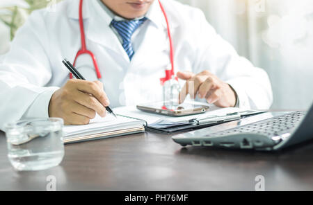 Medico per iscritto le informazioni su notebook e guardando il telefono per la pianificazione di prendersi cura buoni e sani Foto Stock