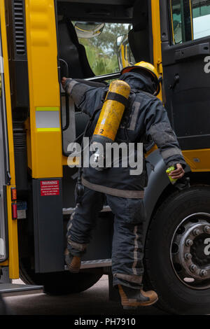 Dietro un vista di un vigili del fuoco scendendo da un giallo motore fire con vi pieno uniforme e serbatoio di ossigeno su Foto Stock