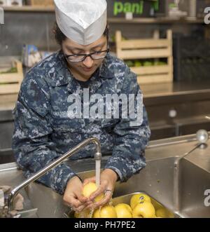 Mare Mediterraneo (24 giugno 2018) Engineman Fireman Diana Maldonado, da Austin, Texas, lava le mele in cucina a bordo del San Antonio-classe di trasporto anfibio dock nave USS New York (LPD) 21 giugno 24, 2018. New York, homeported a Mayport, Florida, sta conducendo operazioni navali negli Stati Uniti Sesta flotta area di operazioni a sostegno degli Stati Uniti per gli interessi di sicurezza nazionali in Europa e in Africa. Foto Stock