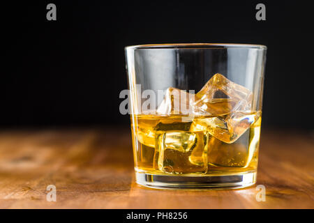 Bicchiere di bibita alcolica con cubetti di ghiaccio su un tavolo di legno. Whiskey in vetro. Foto Stock
