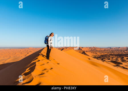 La donna si erge su un dune di sabbia rossa nel deserto, paesaggio di dune Erg Chebbi, Merzouga, Sahara, Marocco Foto Stock