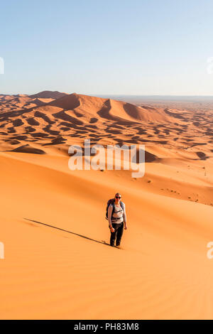 La donna sta nella sabbia sulle dune, dune di sabbia rossa nel deserto, paesaggio di dune Erg Chebbi, Merzouga, Sahara, Marocco Foto Stock