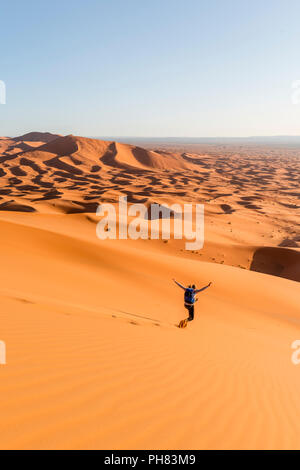 Donna in corsa in discesa, dune di sabbia rossa nel deserto, paesaggio di dune Erg Chebbi, Merzouga, Sahara, Marocco Foto Stock