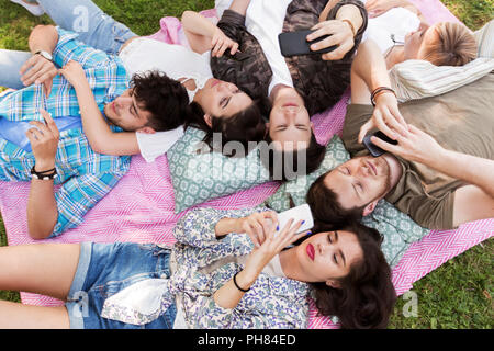 Gli amici con gli smartphone sulla coperta picnic Foto Stock