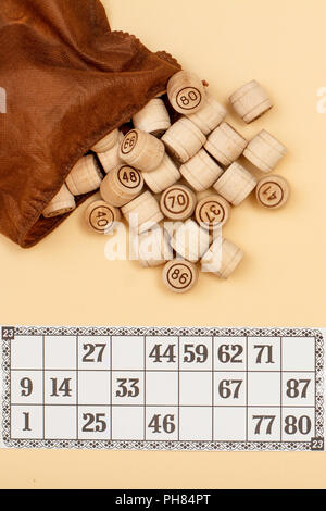 Lotto in legno Barili con borsa marrone e scheda di gioco su sfondo beige. Gioco di bordo del lotto. Vista superiore Foto Stock