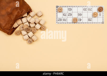 Lotto in legno Barili con borsa marrone e scheda di gioco su sfondo beige. Gioco di bordo del lotto. Vista da sopra con lo spazio di copia Foto Stock