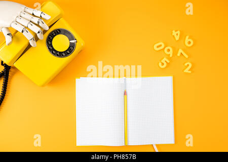 Tagliate il colpo di mano robotica di raggiungere per telefono vintage giallo sul piano portapaziente con il notebook in bianco e numeri di matematica Foto Stock