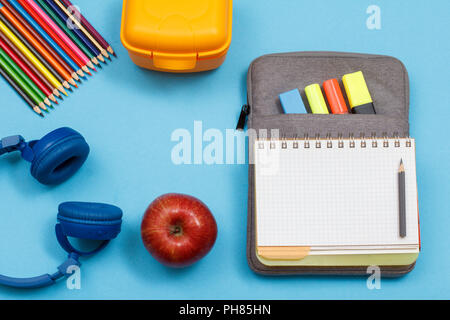 Cuffie, matite colorate, scatola di pranzo, Apple, aprire il quaderno sul sacchetto custodia a matita con colore pennarelli e un marcatore su sfondo blu. Vista dall'alto. Indietro Foto Stock