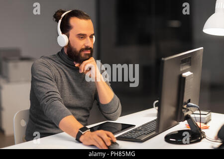 Uomo creativo nelle cuffie lavorando di notte office Foto Stock