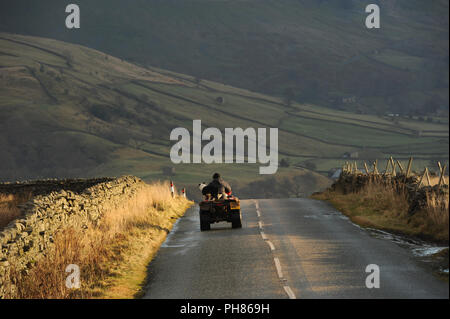 Un allevatore di pecore guida un quad con il suo cane collie alto su Buttertubs Pass - inverno nelle Yorkshire Dales, Inghilterra Foto Stock