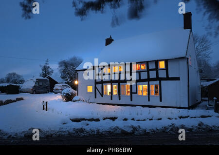 La neve pesante cade su un cottage bianco e nero a Longnor, Shropshire. Preso al crept con le luci della casa che illuminano e che riflettono sulla neve fuori. Cottage di proprietà del fotografo Foto Stock