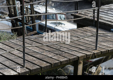 In legno rustico jetty al punto di ormeggio per imbarcazioni da diporto a Skippool Creek sul fiume Wyre nel Lancashire, Inghilterra, Regno Unito con la barca in background. Foto Stock