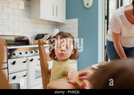 Punto di vista angolo di una bambina di essere consegnati alcuni alimenti al tavolo della cucina. La bambina è focalizzato sul cibo e ha le briciole intorno a lei mou Foto Stock