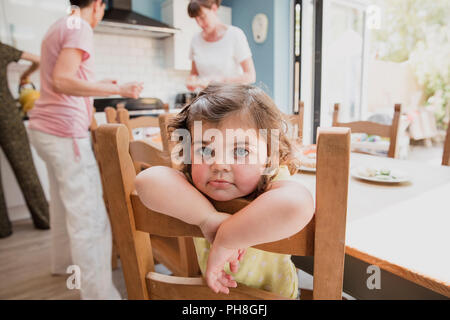Poco ragazza seduta appeso fuori il retro di un tavolo da pranzo sedia in cucina. La bambina è seduto in attesa per il suo pranzo per essere realizzato. Foto Stock