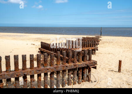 Di ferro arrugginito storm barriere di difesa su una sabbiosa spiaggia di Norfolk nel Regno Unito zigzagando verso il mare. Foto Stock