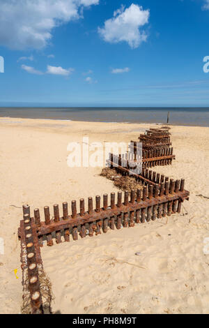 Di ferro arrugginito storm barriere di difesa a zig-zag lungo la sabbiosa spiaggia di Norfolk in Inghilterra del sud Foto Stock